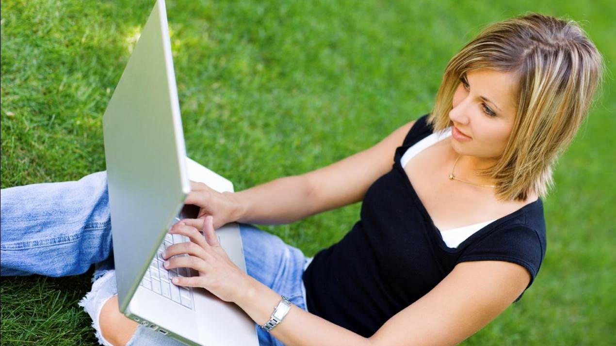 woman typing on a laptop sitting in the grass
