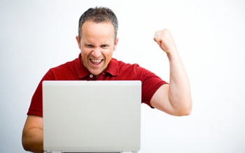 excited man looking at laptop with fist in the air